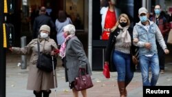 People wearing protective masks wait to cross the road, as the coronavirus disease (COVID-19) outbreak continues, in Manchester, Britain, Oct. 19, 2020. 