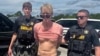 FILE - Ryan W. Routh, suspected of attempting to assassinate former President Donald Trump, stands handcuffed between two Martin County deputies after his arrest near Palm City, Florida, Sept. 15, 2024. (Martin County Sheriff's Office/Handout via Reuters)