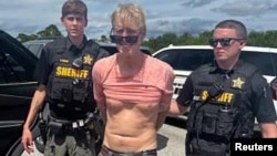 Ryan Wesley Routh, suspected of attempting to assassinate former President Donald Trump, stands handcuffed between two Martin County deputies after his arrest near Palm City, Florida, Sept. 15, 2024. (Martin County Sheriff's Office/Handout via Reuters)