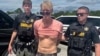 FILE - Ryan W. Routh, suspected of attempting to assassinate former President Donald Trump, stands handcuffed between two Martin County deputies after his arrest near Palm City, Florida, Sept. 15, 2024. (Martin County Sheriff's Office/Handout via Reuters)