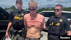 FILE - Ryan W. Routh, suspected of attempting to assassinate former President Donald Trump, stands handcuffed between two Martin County deputies after his arrest near Palm City, Florida, Sept. 15, 2024. (Martin County Sheriff's Office/Handout via Reuters)