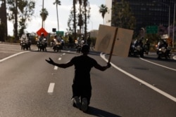 A man kneels on the street in front of police officers while chanting "I can't breathe" during a protest over the death of George Floyd, May 29, 2020, in Los Angeles. Floyd died Memorial Day while in police custody in Minneapolis.