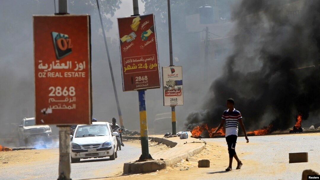 Para pengendara melintas di depan ban-ban yang dibakar sebagai penghalang di tengah demonstrasi untuk mendesak pemerintah memperbaiki kondisi negara di Khartoum, Sudan, Rabu, 21 Oktober 2020. (Foto: Reuters)