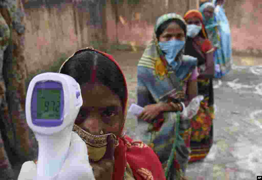 An election officer checks the temperature of a voter before allowing voters to pass at a polling station, during the first phase of state elections at Paliganj, in the eastern Indian state of Bihar.