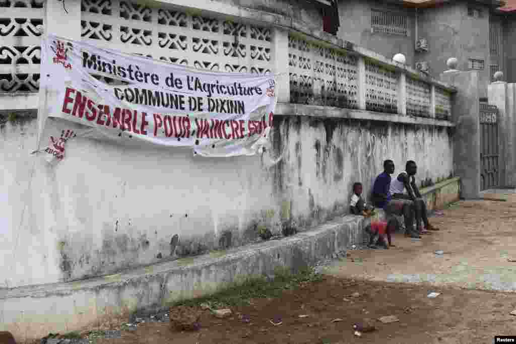 People sit near a banner reading "The Ministry of Agriculture, Dixinn Commune, Together to defeat Ebola," in Conakry, Guinea, Oct. 26, 2014.