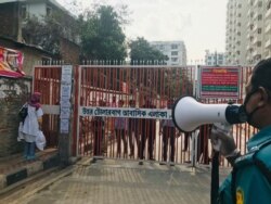 FILE - A policeman urges residents not to come out of their homes as residents stand behind a gate, hours after the second death from COVID-19 was confirmed from the area, in Dhaka, Bangladesh, March 23, 2020.