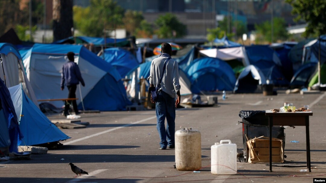 FILE - Migrants walk in a camp set by the Baobab aid group in Rome, Italy, July 12, 2018.