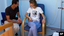 This photo posted Aug 8, 2018 on the official Facebook page of the Syrian Presidency, shows President Assad sitting next to his wife Asma Assad with an IV in her left arm in what appears to be a hospital room, in Syria. 