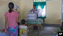 FILE - Voters wait in line as a man casts his ballot at a polling station in Dala township in Yangon, Myanmar, December 2014.