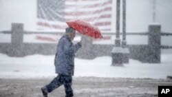 A pedestrian passes in front of an American flag as snow falls in Manchester, N.H., Feb. 5, 2016. 