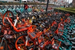 A man wearing a protective face mask walks by a pile of bicycles from bike-sharing companies parked outside a subway station in Beijing, March 2, 2020.
