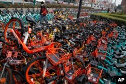 A man wearing a protective face mask walks by a pile of bicycles from bike-sharing companies parked outside a subway station in Beijing, March 2, 2020.