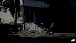 FILE: A woman walks past a building destroyed in Russian shelling in Borodyanka, on the outskirts of Kyiv, Ukraine, Tuesday, 6.21.2022