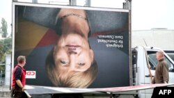 Employees of a billboard advertising company carry a disassembled election poster of Germany's Christian Democratic Union (CDU) party with the portrait of German Chancellor Angela Merkel in Berlin on Sept. 25, 2017.