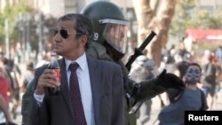 FILE - A man drinks a Frucola as a police officer chases demonstrators during a protest against Chile's government in Santiago, Chile, Dec. 4, 2019. 