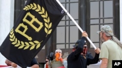 FILE - A protester carries a banner of the Proud Boys, a right-wing group, while other members start to unfurl a large U.S. flag in front of the Oregon State Capitol in Salem, Sept. 7, 2020. 