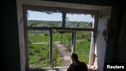 Un militaire ukrainien inspecte la zone depuis un bâtiment endommagé par une frappe militaire russe dans la ville de Marinka, dans la région de Donetsk, Ukraine le 28 mai 2022. 