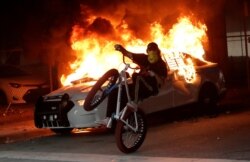 Un manifestante en bicicleta pasa junto a un auto incendiado de la policía durante una protesta cerca del Departamento de Policía de Miami, el sábado 30 de mayo de 2020.