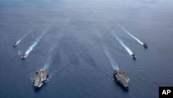 In this photo provided by U.S. Navy, the USS Ronald Reagan (CVN 76) and USS Nimitz (CVN 68) Carrier Strike Groups steam in formation, in the South China Sea, July 6, 2020. 
