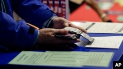 FILE - a voter shows his photo identification to an election official at an early voting polling site, in Austin, Texas.