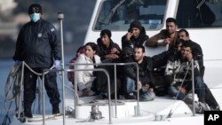 FILE - A Greek coast guard officer, wearing a mask for fear of infectious disease, stands next to a small group of immigrants on a launch carrying them to shore from a crippled ship holding more than 700 people at the coastal Cretan port of Ierapetra, Greece, Nov. 27, 2014. 