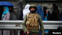 A policeman stands guard outside a polling station in Kabul as Afghans wanting to vote queue outside before it opens, April 5, 2014. 