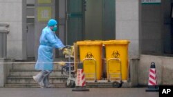 Staff move bio-waste containers past the entrance of the Wuhan Medical Treatment Center, where some infected with a new virus are being treated, in Wuhan, China, Wednesday, Jan. 22, 2020. (AP Photo/Dake Kang)