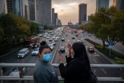 Women wearing face masks to protect against the coronavirus stand on a pedestrian bridge in Beijing, Nov. 13, 2020.