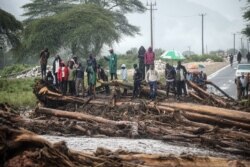 FILE - People stand on debris blocking a highway after River Muruny burst its bank following heavy rains in Parua village, about 85 km northeast of Kitale, in West Pokot county, western Kenya, Nov. 24, 2019.