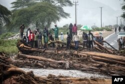 FILE - People stand on debris blocking a highway after River Muruny burst its bank following heavy rains in Parua village, about 85 km northeast of Kitale, in West Pokot county, western Kenya, Nov. 24, 2019.