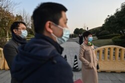People wearing face masks stand next to an access area of the Hilton Wuhan Optics Valley Hotel where members of a World Health Organization team, investigating the origins of the coronavirus pandemic, are staying in Wuhan, China, Jan. 28, 2021.