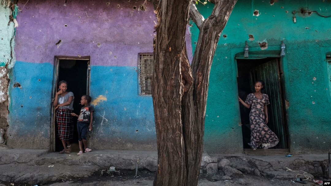 FILE - People stand at the doors of houses that were damaged by shelling in the town of Mehoni, in Southern Tigray, Ethiopia, Dec. 11, 2020. 