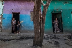 FILE - People stand at the doors of houses that were damaged by shelling in the town of Mehoni, in southern Tigray, Ethiopia, Dec. 11, 2020.