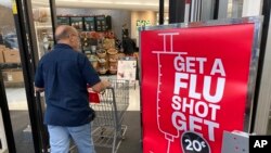 In this Wednesday, Oct. 6, 2021, photograph, a shopper passes a sign urging people to get a flu shot outside a Hy-Vee grocery store in Sioux City, Iowa. (AP Photo/David Zalubowski)