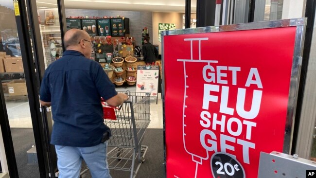 In this Wednesday, Oct. 6, 2021, photograph, a shopper passes a sign urging people to get a flu shot outside a Hy-Vee grocery store in Sioux City, Iowa. (AP Photo/David Zalubowski)