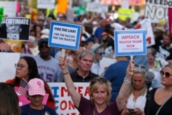 Protesters hold signs during a "We Stand Up" gathering, protesting a rally by President Donald Trump, Aug. 1, 2019, in Cincinnati.