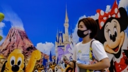 A woman in Tokyo wears a protective mask as she passes Tokyo Disneyland.