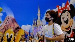 A woman in Tokyo wears a protective mask as she passes Tokyo Disneyland.