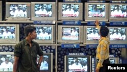 Indian salesman tunes televisions at an electronics shop as government official on screen pledges to boost spending for rural infrastructure, 2006 (file photo).