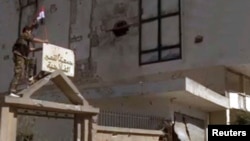 A member of forces loyal to Syria's President Bashar al-Assad erects a Syrian flag atop of a gate in Qusair, June 5, 2013.