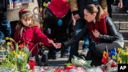 Seorang perempuan dan anak perempuan menyalakan lilin di sebuah memorial untuk para korban bom di Place de la Bourse, Brussels (26/3).(AP/Geert Vanden Wijngaert)