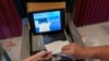 FILE - A polling judge, right, helps guide a voter's ballot into a voting machine during the Pennsylvania primary election at Mont Alto United Methodist Church in Alto, Pennsylvania, on May 17, 2022. 