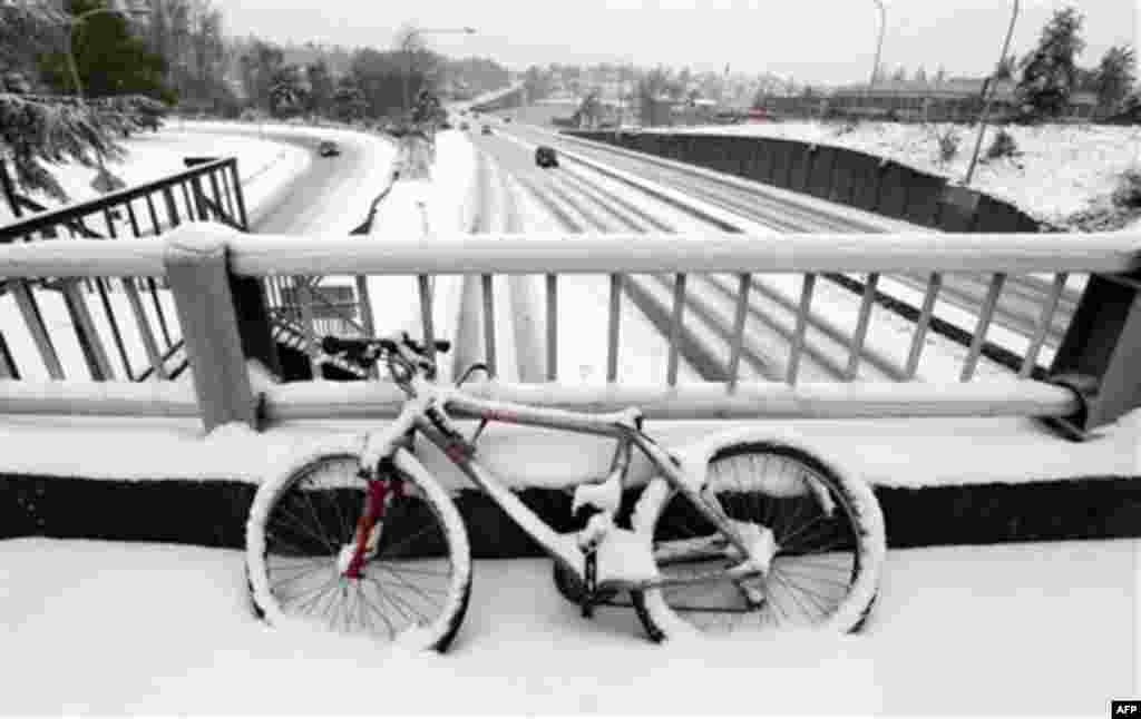 A snow-covered bicycle is locked to a bridge as unusually light traffic drives past below on Highway 520 near the University of Washington Thursday, Jan. 19, 2012, in Seattle. A monster Pacific Northwest storm coated the Seattle area in a thick layer of i