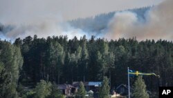 Smoke rises from just beyond a bank of trees and homes, as a wildfire threatens large tracts of land, outside Ljusdal, Sweden, July 17, 2018.