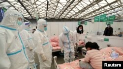Para petugas kesehatan dengan pakaian hazmat memeriksa kondisi pasien anak yang terjangkit COVID-19 yang dirawat di Shanghai New International Exhibition Hall pada 9 April 2022. Gedung Ekshibisi itu kini telah diubah menjadi rumah sakit darurat. (Foto: China Daily via Reuters)