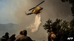 A firefighting helicopter drops water drop as a wildfire burns in the village of Pyrgos, near Corinth, Greece, on September 30, 2024.