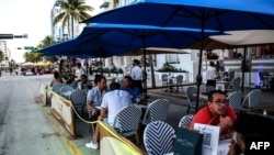 FILE - People eat in an outdoor dining area of a restaurant in Miami Beach, Florida, June 24, 2020. With coronavirus cases surging officials are imposing tough measures.