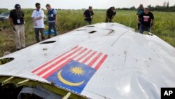 Malaysian investigators along with members of the OSCE mission in Ukraine, examine a piece of the crashed Malaysia Airlines Flight 17 in the village of Petropavlivka, Donetsk region, eastern Ukraine, July 23, 2014.