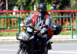 FILE - A man wearing a tear gas mask drives his motorcycle during a lockdown order by the Albanian government to prevent the spread of the new coronavirus in Tirana, April 9, 2020.