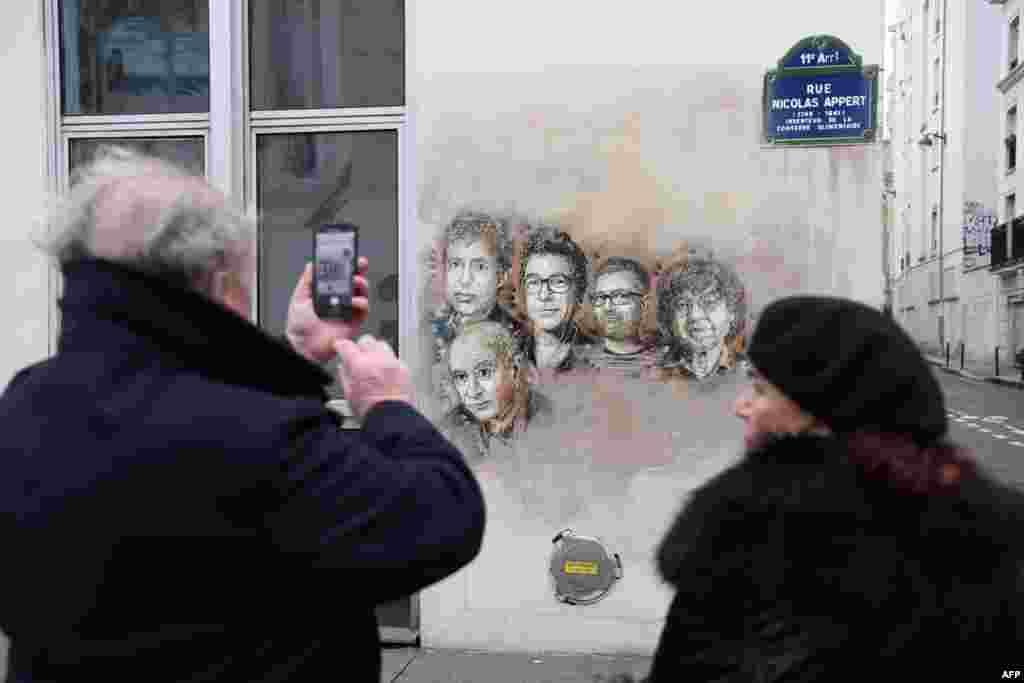 A man takes a picture of portraits (LtoR) of late French satirical weekly Charlie Hebdo&#39;s deputy chief editor Bernard Maris, French cartoonists Georges Wolinski, Bernard Verlhac (aka Tignous), Charlie Hebdo editor Stephane Charbonnier (aka Charb) and Jean Cabut (aka Cabu) near the magazine&#39;s offices at Rue Nicolas Appert, in Paris on the third anniversary of the jihadist attack on French satirical magazine Charlie Hebdo.
